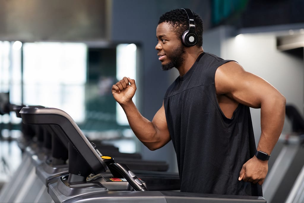 man smiling while running on treadmill listening to headphones having fun at gym