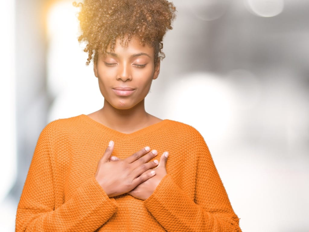 young woman holding hands over heart feeling gratitude - how to be more grateful